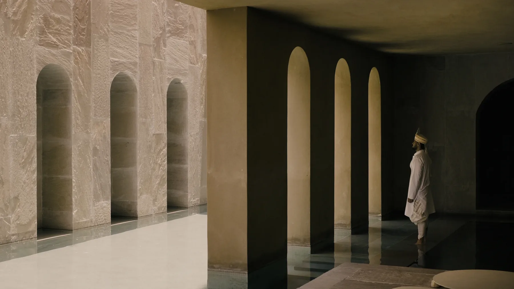 A figure in white walking the length of the arcade, the arches repeated in the polished floor
