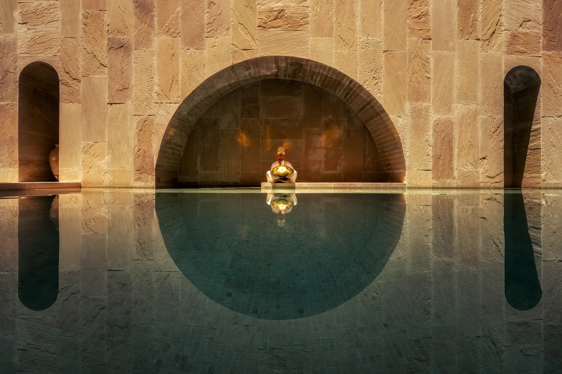 The seated figure within the stone arch, reflected in the courtyard pool