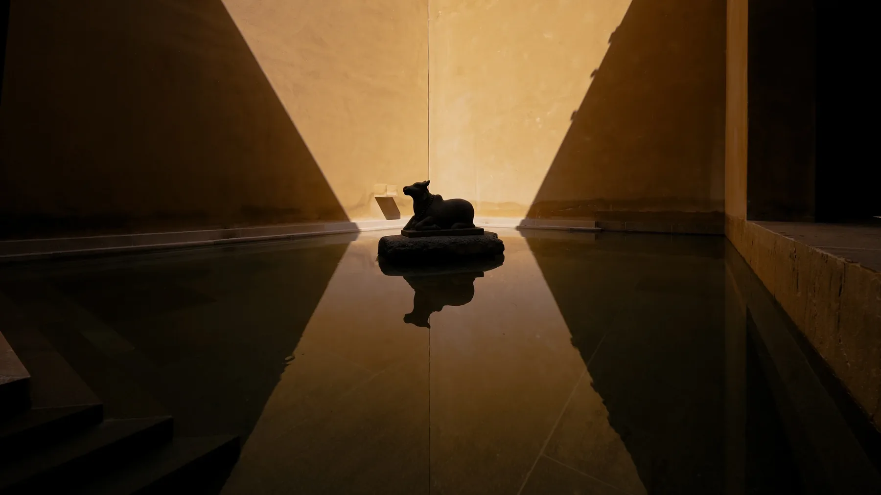 A low-lit corridor with a figure silhouetted on a plinth and mirrored in the polished floor