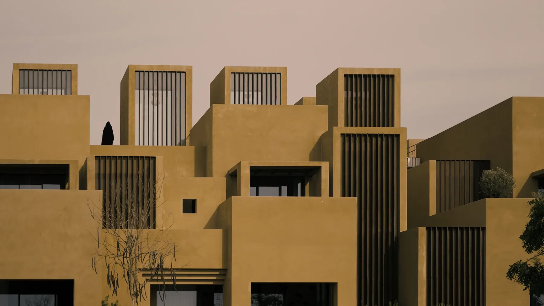 The villa read from outside as a composition of stacked ochre volumes, a figure standing on one of the upper terraces