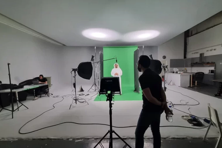 BTS image from a green screen film shoot showing crew, gear, and chroma key background in studio environment
