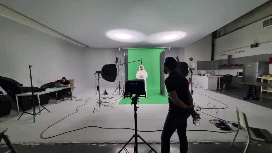 BTS image from a green screen film shoot showing crew, gear, and chroma key background in studio environment